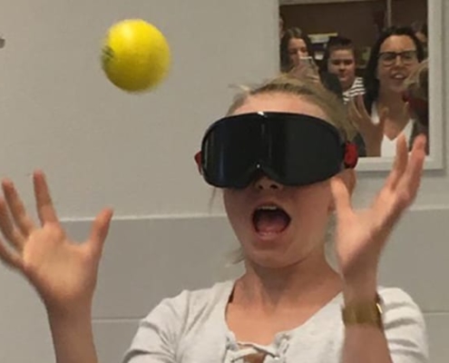 Schülerin testet ihr Reaktionsvermögen mit dunkler Brille und Tennisball